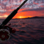 A red, orange, yellow and purple sunset over the ocean, with a fishing pole in the center.