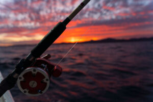 A red, orange, yellow and purple sunset over the ocean, with a fishing pole in the center.