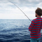 Young man fishing in open sea from sail boat