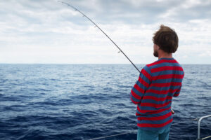 Young man fishing in open sea from sail boat
