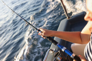 Waiting for catching fish man hand holds a fishing rod with fishing line while sitting in boat. Sea fishing and hobby
